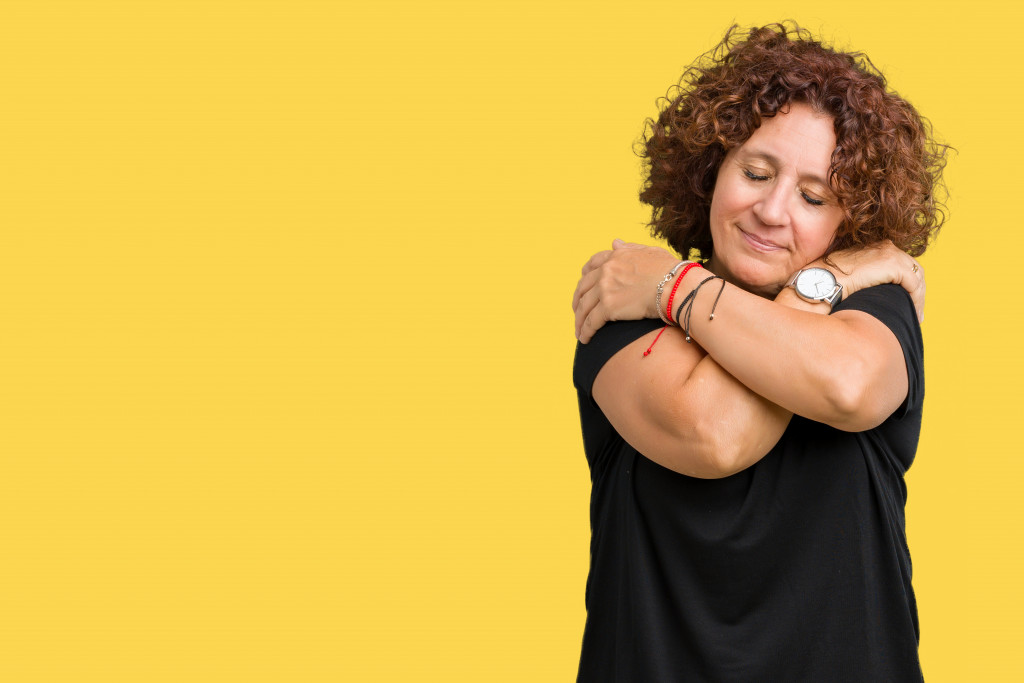 A mature woman hugging herself in front of a yellow background